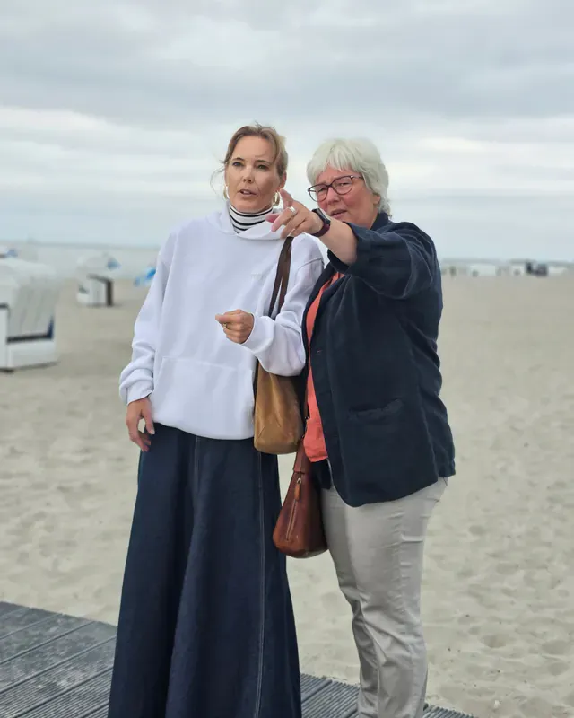 Inken Kuhn zeigt am Ostseestrand auf etwas in der Ferne, neben ihr eine Frau.